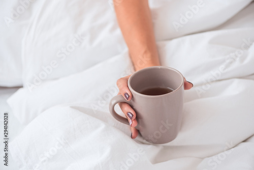 Woman hand hold cup of tea on the bed