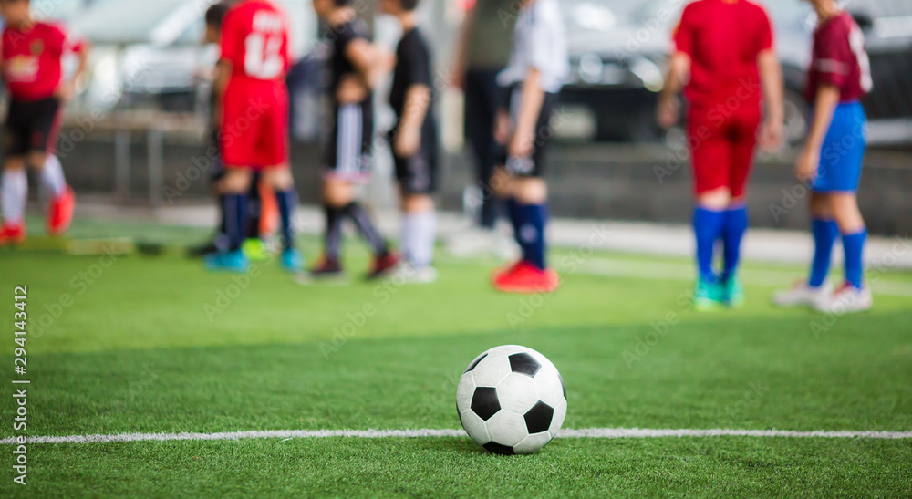 Soccer ball on green artificial turf with blurry soccer team training. Blurry kid player training and soccer equipment in soccer academy. Soccer ball on green artificial turf with blurry soccer team training. Blurry kid player training and soccer equipment in soccer academy.