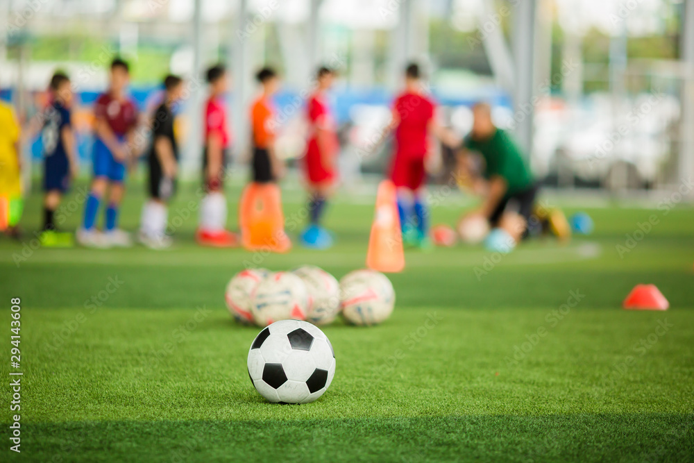 Soccer ball on green artificial turf with blurry soccer team training. Blurry kid player training and soccer equipment in soccer academy.