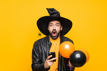 Man with witch hat holding black and orange air balloons for halloween party surprised and sending a message