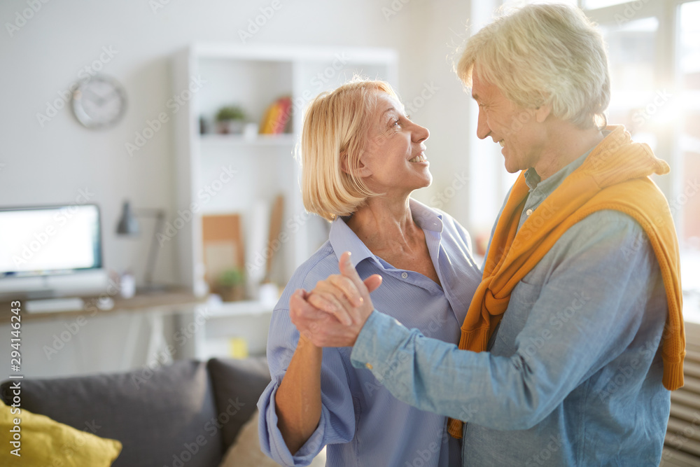Side view portrait of loving senior couple slow dancing in living room lit by sunlight, copy space Side view portrait of loving senior couple slow dancing in living room lit by sunlight, copy space