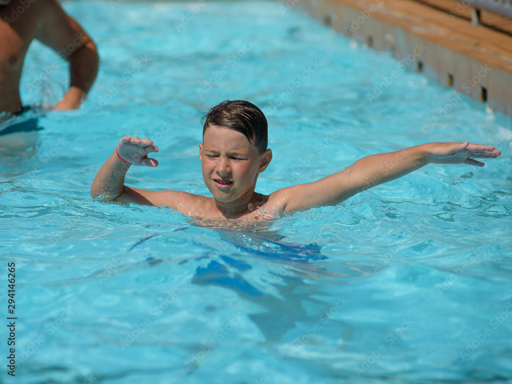 Cute European boy dancing aqua Zumba in hotel’s pool during his summer vacations. Healthy active childhood concept.