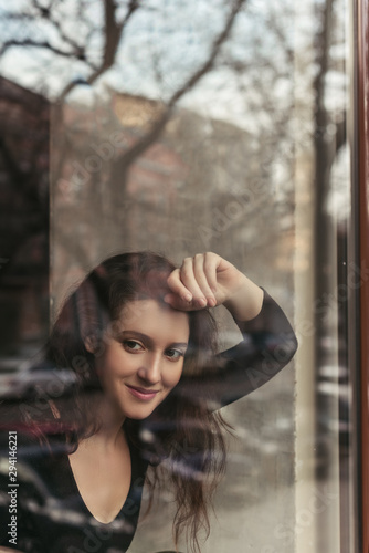 Portrait of a beautiful smiling brunette sitting in a coffee house behind a glass, a concept of femininity and natural beauty, a lifestyle