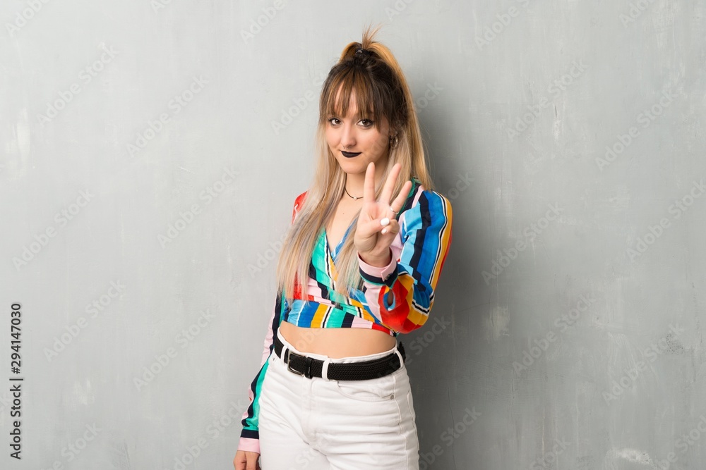 Young girl with colorful clothes happy and counting three with fingers Young girl with colorful clothes happy and counting three with fingers