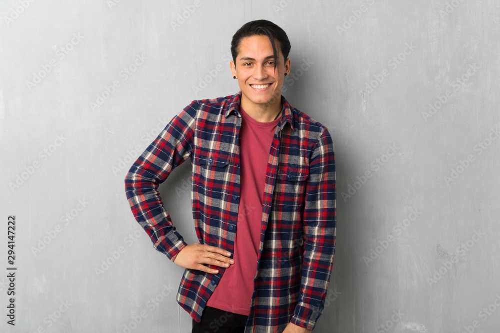 Man over grunge wall posing with arms at hip and smiling Man over grunge wall posing with arms at hip and smiling