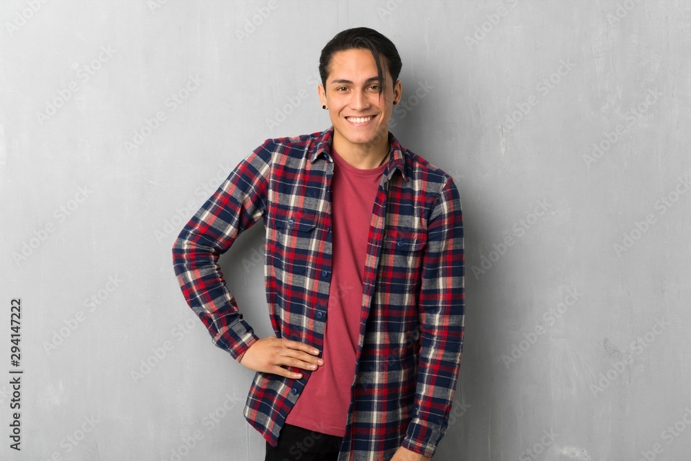 Man over grunge wall posing with arms at hip and smiling