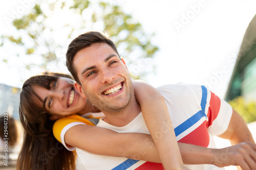 happy boyfriend and girlfriend piggyback outdoors