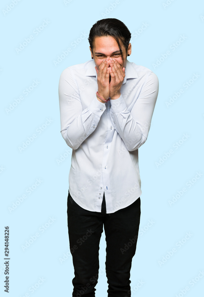 Handsome man smiling a lot while covering mouth over isolated blue background
