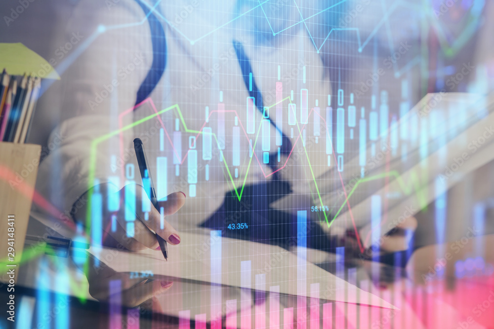 A woman hands writing information about stock market in notepad. Forex chart holograms in front. Concept of research. A woman hands writing information about stock market in notepad. Forex chart holograms in front. Concept of research.