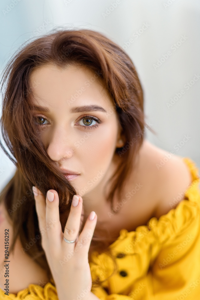 Portrait of smiling beatiful young woman with long brunette hair and big brown eyes in yellow dress is looking at the camera Portrait of smiling beatiful young woman with long brunette hair and big brown eyes in yellow dress is looking at the camera