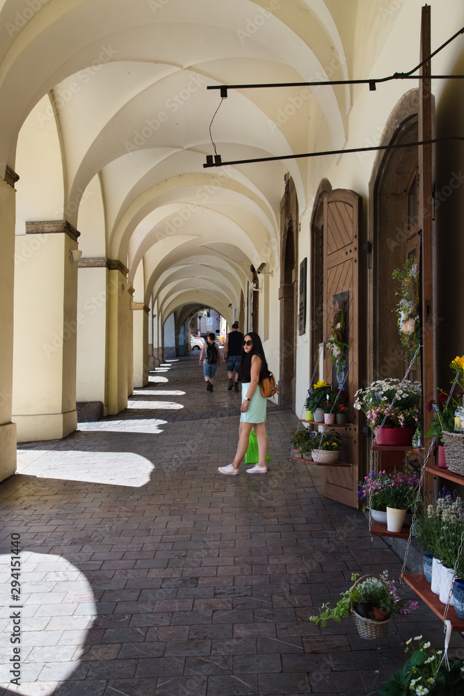 Young brunette woman is standing on cobbled pavement. Arched architecture, Wooden doors and flower shop. Travel to Europe.
