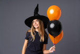 Young witch holding black and orange air balloons laughing and looking up