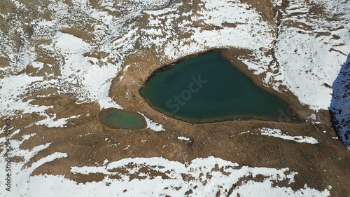 Mountain lake among the snowy peaks. Moraine lake Titova, in the mountains of Almaty, Kazakhstan. Height 3377 m. Shooting with a drone. Yellow rocks, white clouds, snow and blue sky. Highest peak. photo