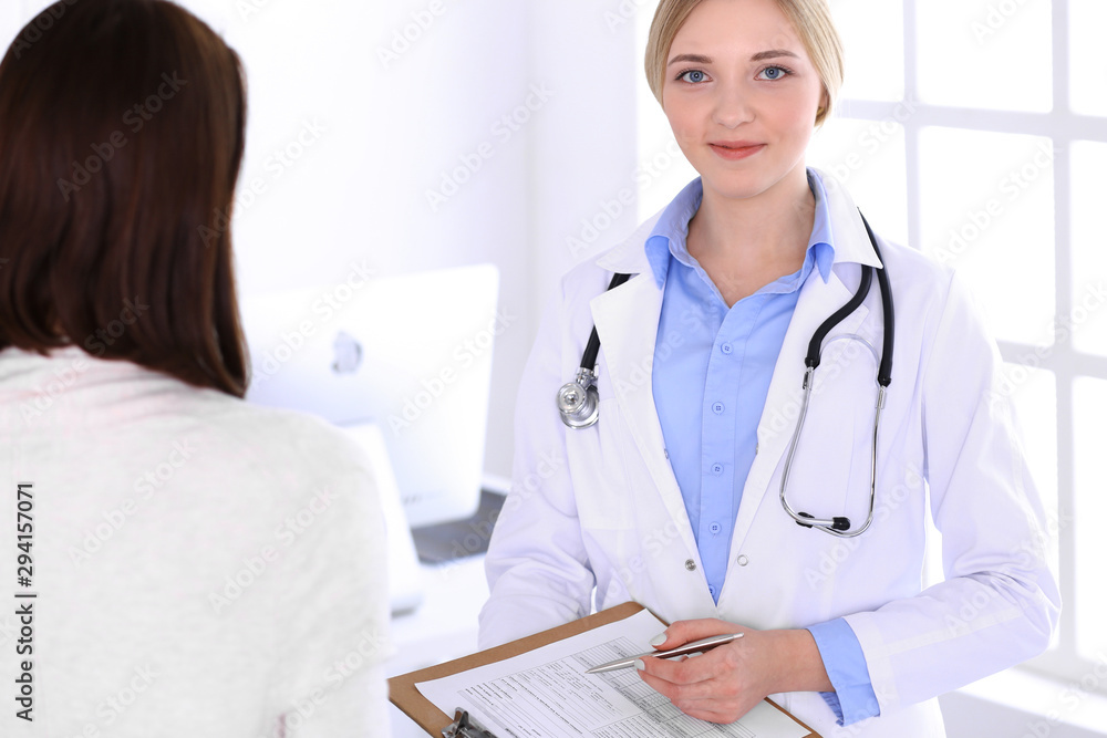 Young woman doctor and patient at medical examination at hospital office. Blue color blouse of therapist looks good. Medicine and healthcare concept Young woman doctor and patient at medical examination at hospital office. Blue color blouse of therapist looks good. Medicine and healthcare concept