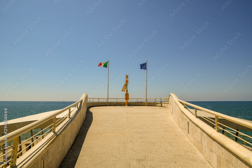 End of the modern pier of Lido di Camaiore, leaned out on the Tyrrhenian Sea in the Tuscany coast with an Italian flag and an European flag in summer, Lucca, Tuscany, Italy