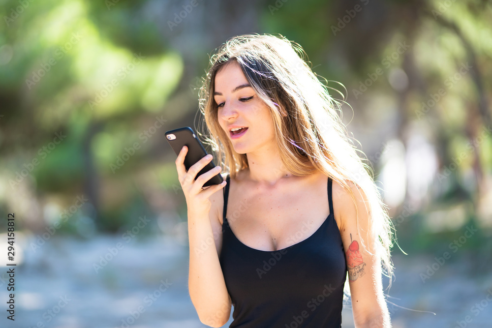 Young girl at outdoors sending a voice message with de phone