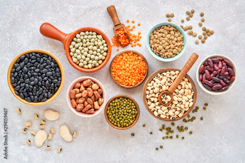 Legumes, lentils  and beans assortment in different bowls on light stone background . Top view. Healthy vegan protein food. photo