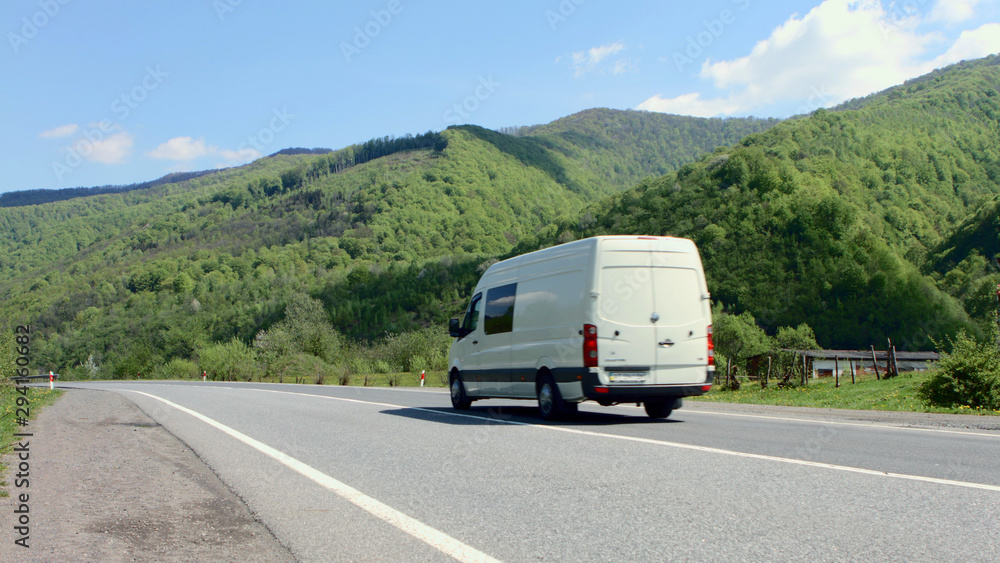 White van traveling at speed on the roads against the backdrop of mountains and pure summer sky