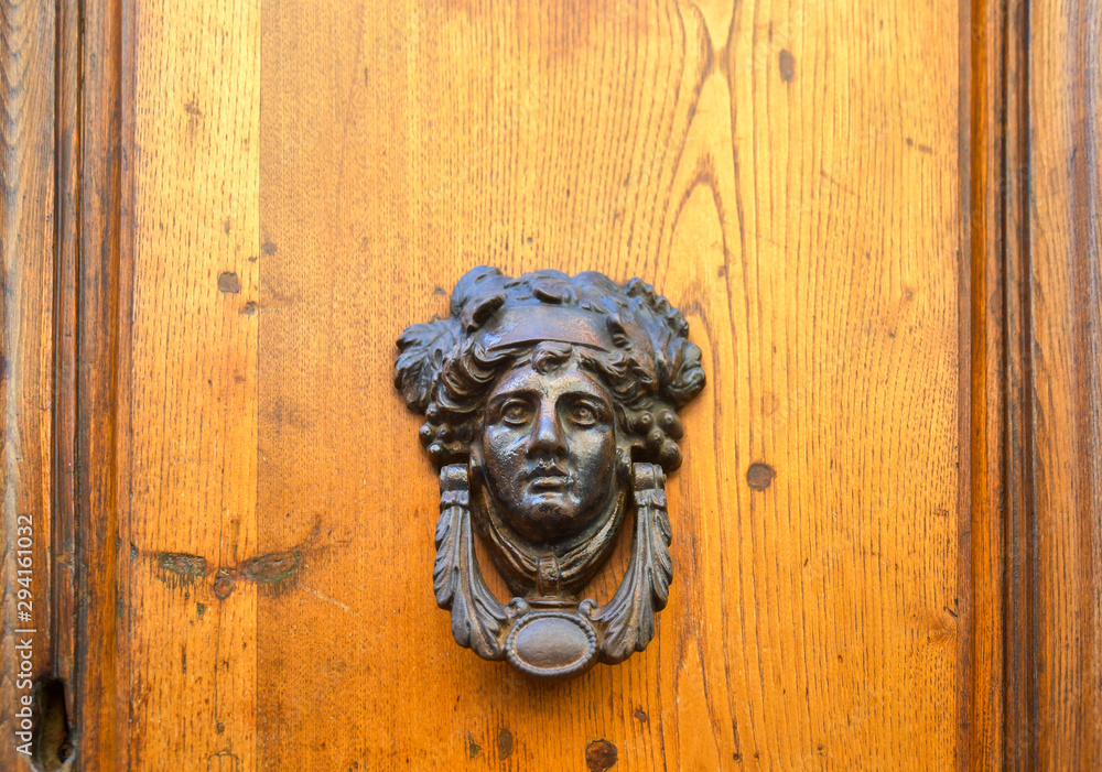 Close-up of a wooden door with an old knocker of cast iron depicting the Greek sun god Apollo with a laurel wreath, Tuscany, Italy