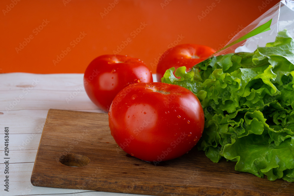 Red tomatoes with water droplets and green lettuce are on a wooden board. Red tomatoes with water droplets and green lettuce are on a wooden board.