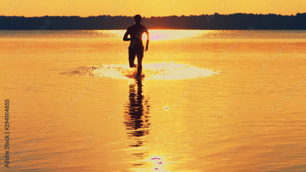 Topless Athletic Muscular And Healthy Man Running In Water Splashing Water During Sunset