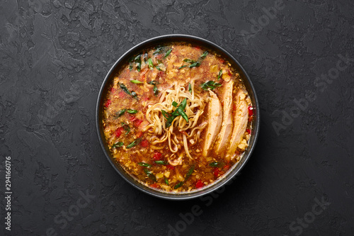 Chicken Manchow Soup in black bowl at dark slate background. Chicken Manchow Soup is indo-chinese cuisine dish with bell peppers, cabbage, carrot, noodles, chilli, soy sauce, green onion and chicken 