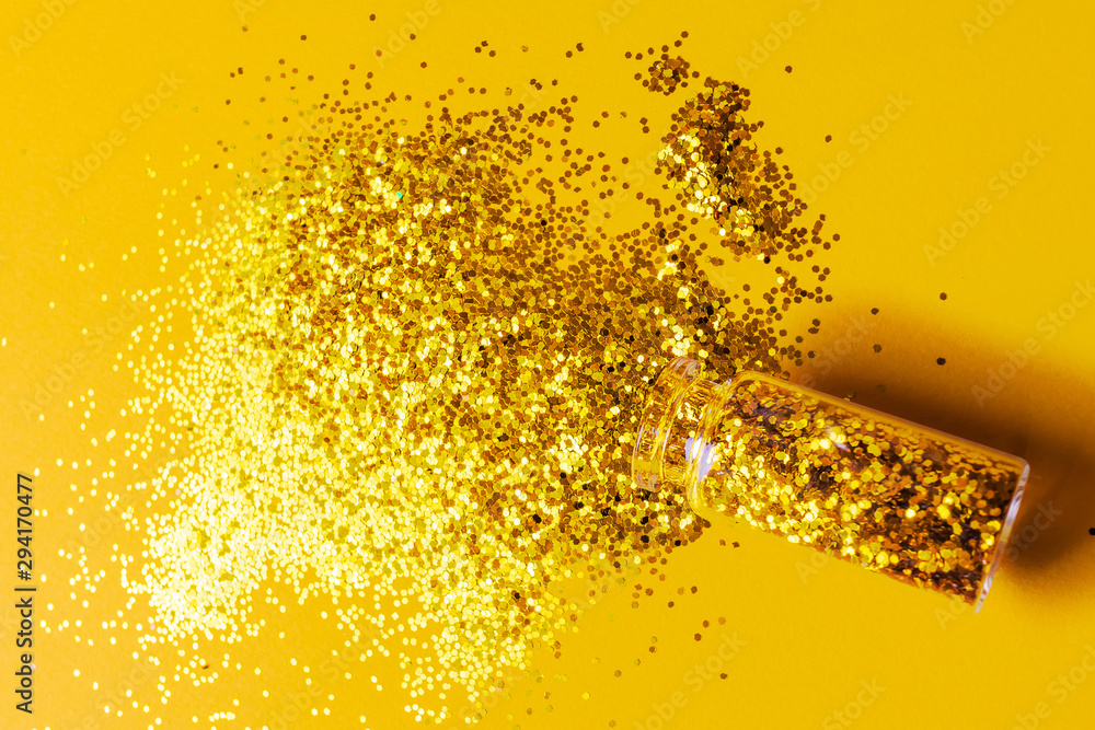 Festive New Year flat lay: golden sparkles in a transparent bottle on a bright yellow background. Minimalism, top view, design, monochrome.