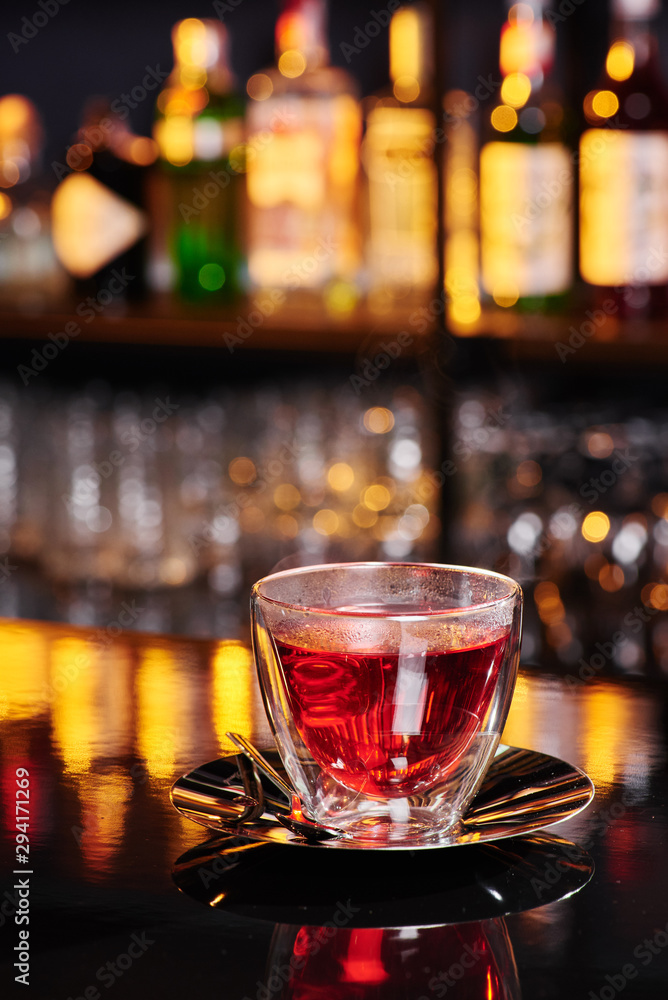 Beautiful transparent cup with red fruit tea on a shiny dark table on a blurred bar background. Close-up. Space Beautiful transparent cup with red fruit tea on a shiny dark table on a blurred bar background. Close-up. Space