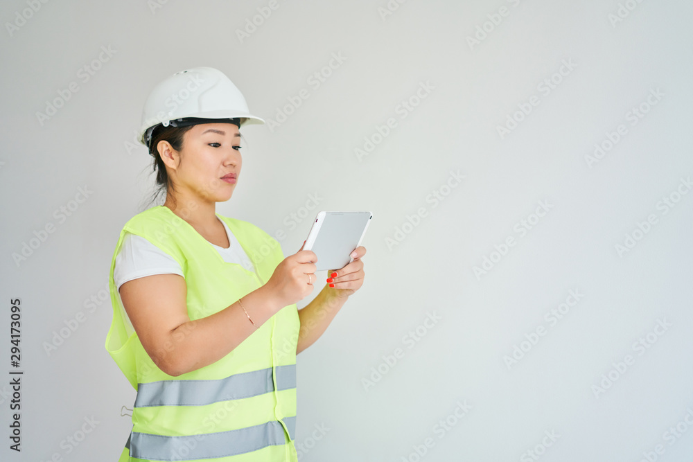Repairs in the apartment, a girl in a green vest and a white helmet is in a white room with a tablet in her hands, the girl makes repairs Repairs in the apartment, a girl in a green vest and a white helmet is in a white room with a tablet in her hands, the girl makes repairs