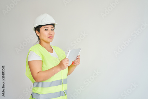 Repairs in the apartment, a girl in a green vest and a white helmet is in a white room with a tablet in her hands, the girl makes repairs