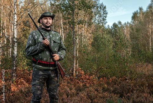 Hunter man in camouflage with a gun during the hunt in search of wild birds or game on the background of the autumn forest. Autumn hunting season. The concept of a hobby, killing.