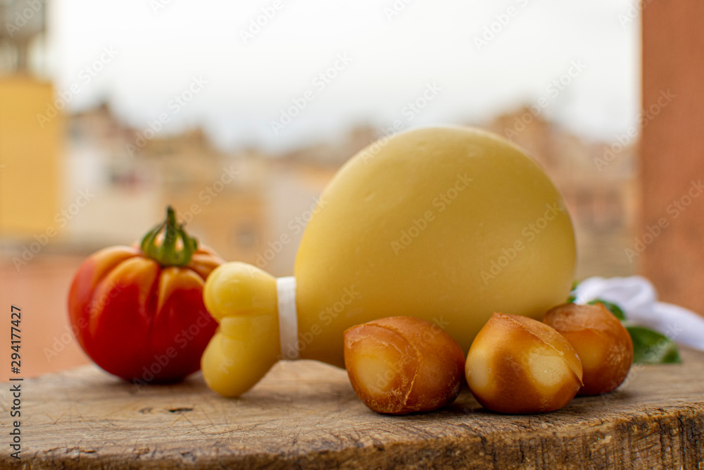 Italian provolone caciocavallo aged and smoked cheeses in teardrop form with yellow houises of old Italian town on background Italian provolone caciocavallo aged and smoked cheeses in teardrop form with yellow houises of old Italian town on background