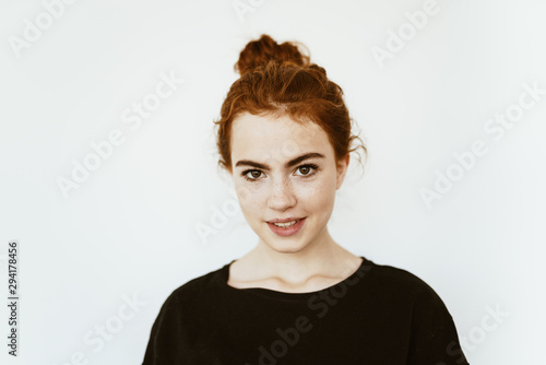 Adorable young girl with curly red hair braided in a bun on her head, with freckles on her face on a white background in a dark jacket cute smiles