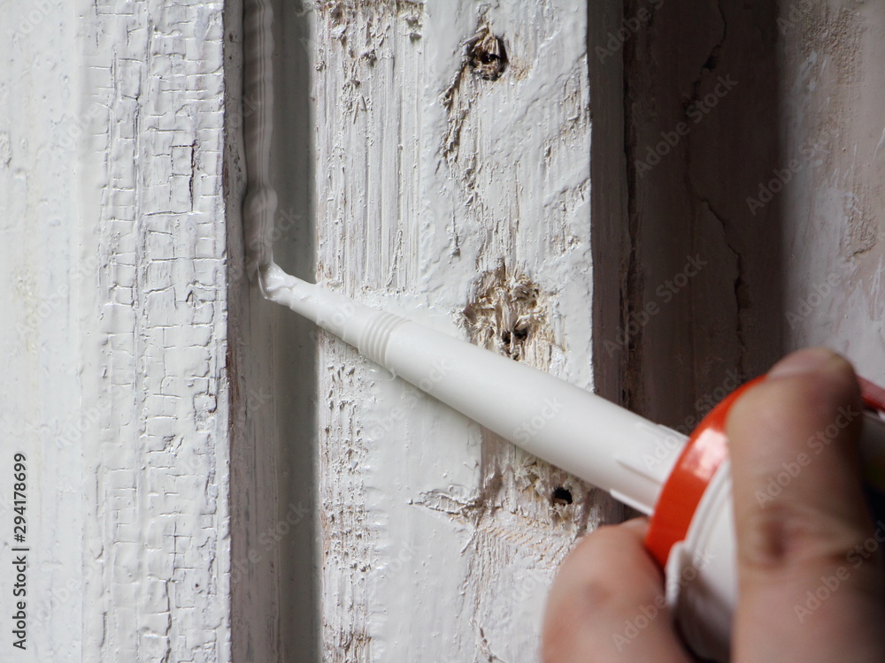 Application of white silicone sealant from a gun to an old painted