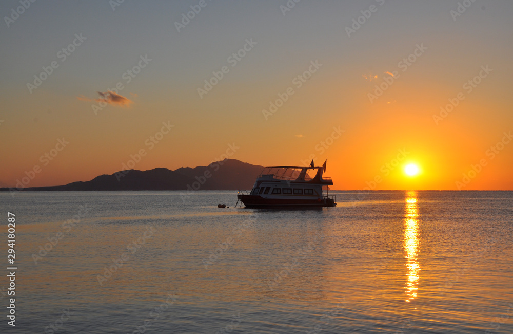 Boat on sunrise in the sea with flags with the island on the background