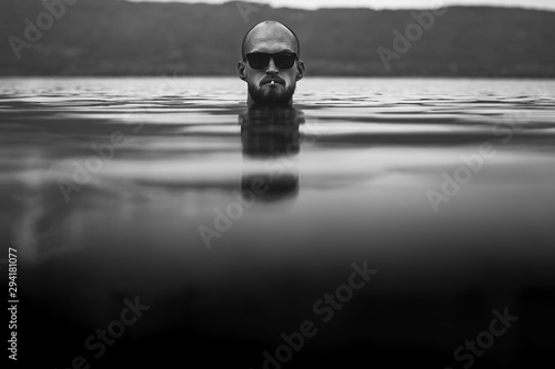 Fényképezés Brutal bearded man with cigarette and in sunglasses emerge in lake