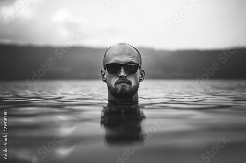 Fotografia Brutal bearded man in sunglasses emerge in lake waves