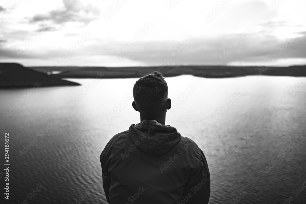 Loneliness concept. Hipster traveler in windbreaker standing alone on top of rock mountain with amazing view on river. Black and white photo. Atmospheric moment. Copy space