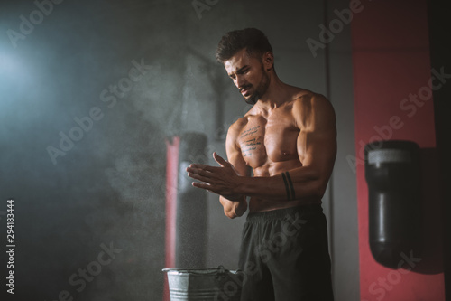 Concentrated bodybuilding man take some powder on his hands and get ready to start a intense workout day in a cross fitness class