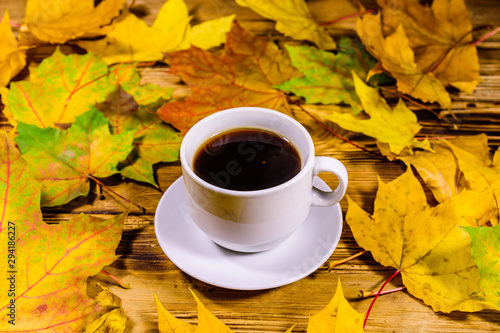 Cup of coffee and heap of yellow maple leaves on a wooden table