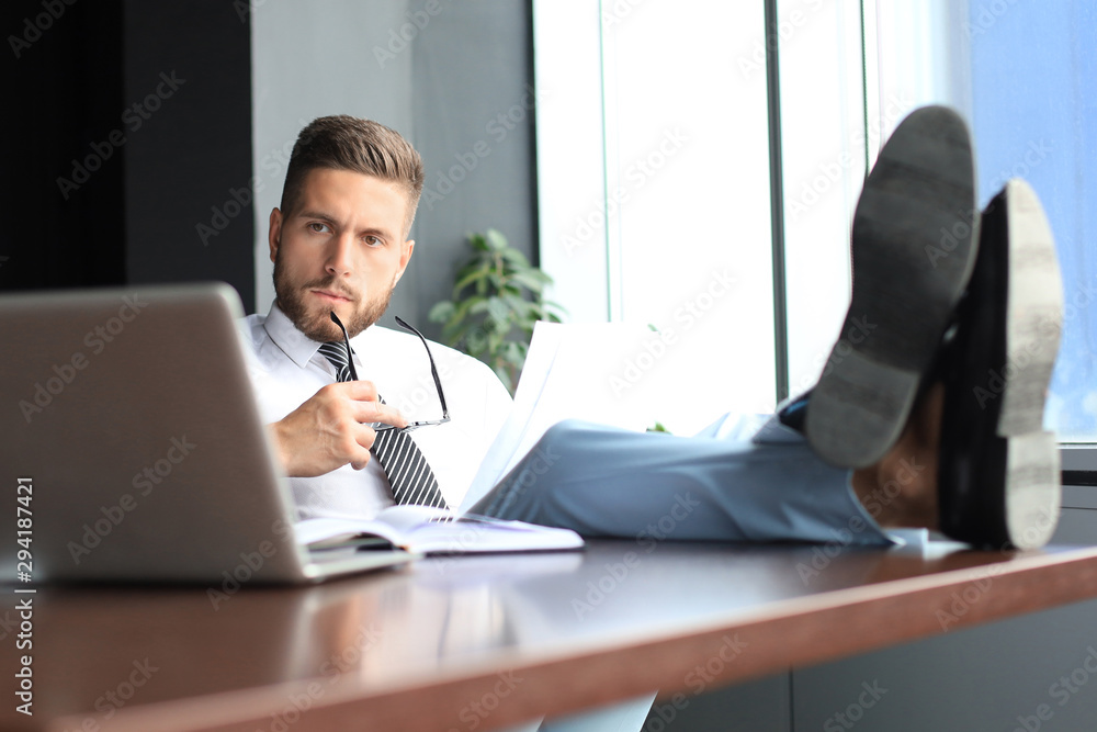 Handsome businessman sitting with legs on table and examing documents in office Handsome businessman sitting with legs on table and examing documents in office