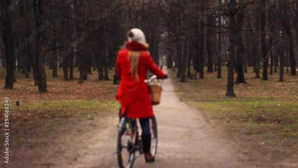 Woman in red winter clothing cycling away at a park autumn season, medium shot