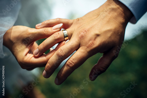 Young bride put a gold wedding ring on the groom's finger, close-up. Wedding ceremony, exchange of rings. On the hand of man wearing a wedding ring.
