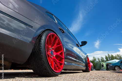 Gray car with lowered suspension and bright red forged wheels is on the parking. Against blue sky