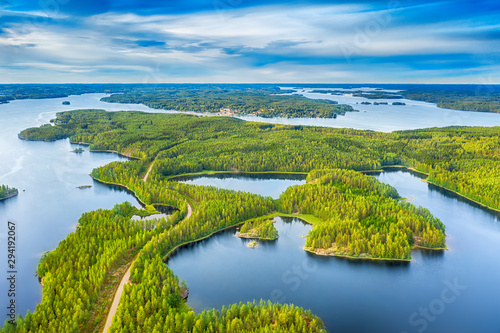 Aerial view of road between green summer forest and blue lake in Finland