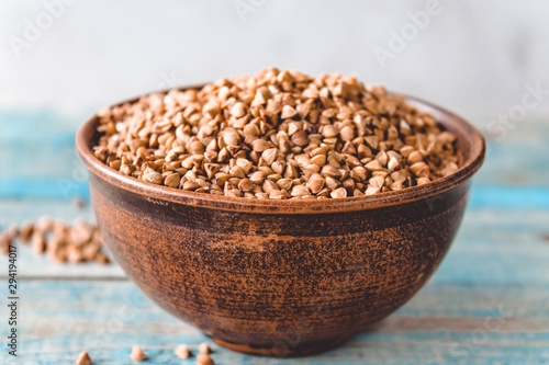 Uncooked buckwheat in a bowl on old boards. Buckwheat is used for cooking. photo