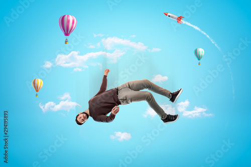 Man in casual clothes with hot air balloons and silver red space rocket in the air on blue background