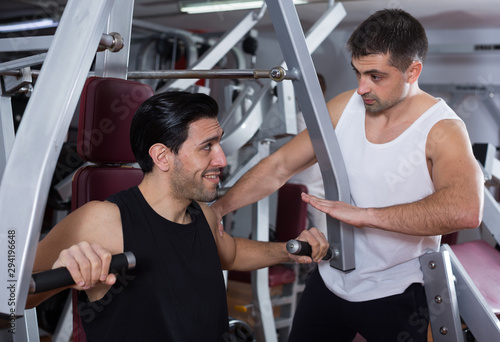Man helping friend on fitness machine in gym