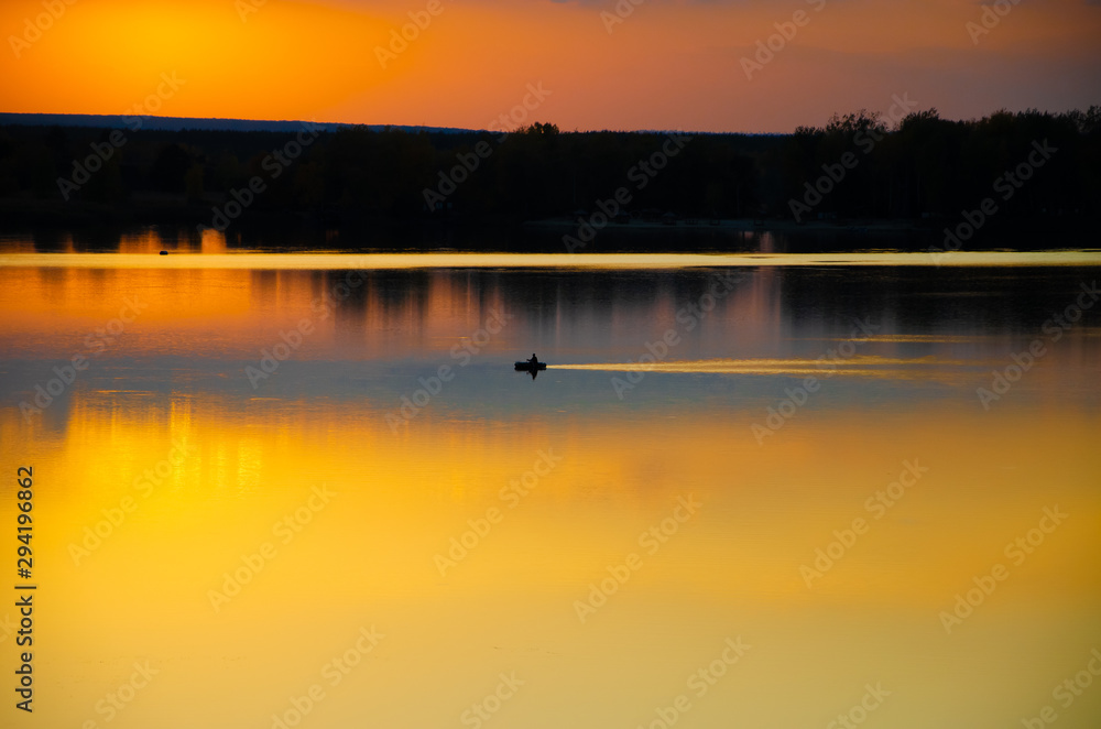 Naklejka premium sunset on the lake and the boatman swims