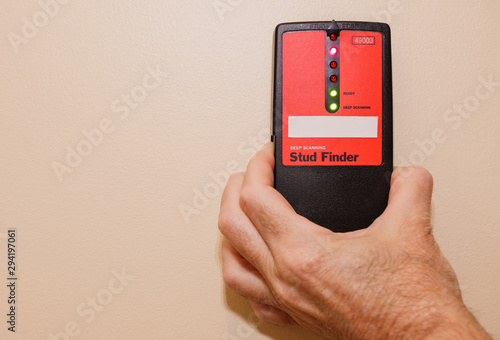 Male carpenter using electronic stud finder to locate interior wall stud.